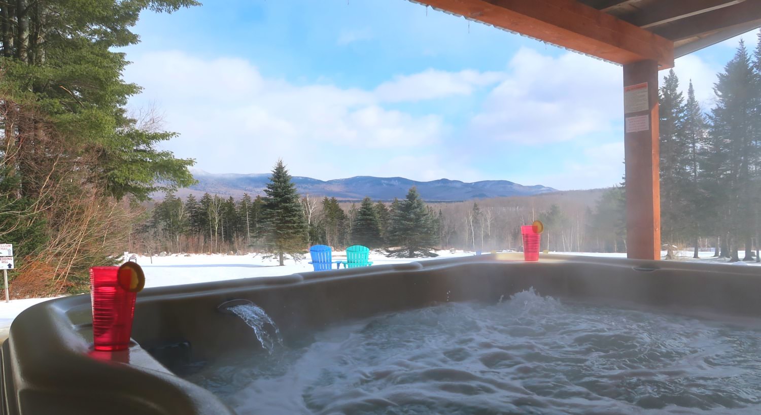 View from bubbling hot tub of snow-covered ground and trees and hills in the background