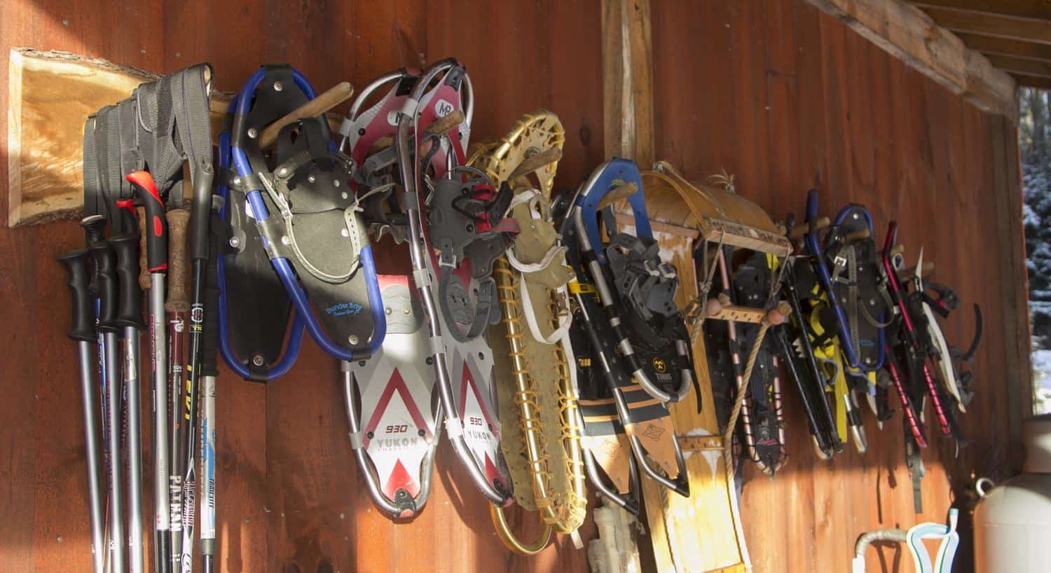 Assorted snowshoes and skis hanging from a  wood cabin wall