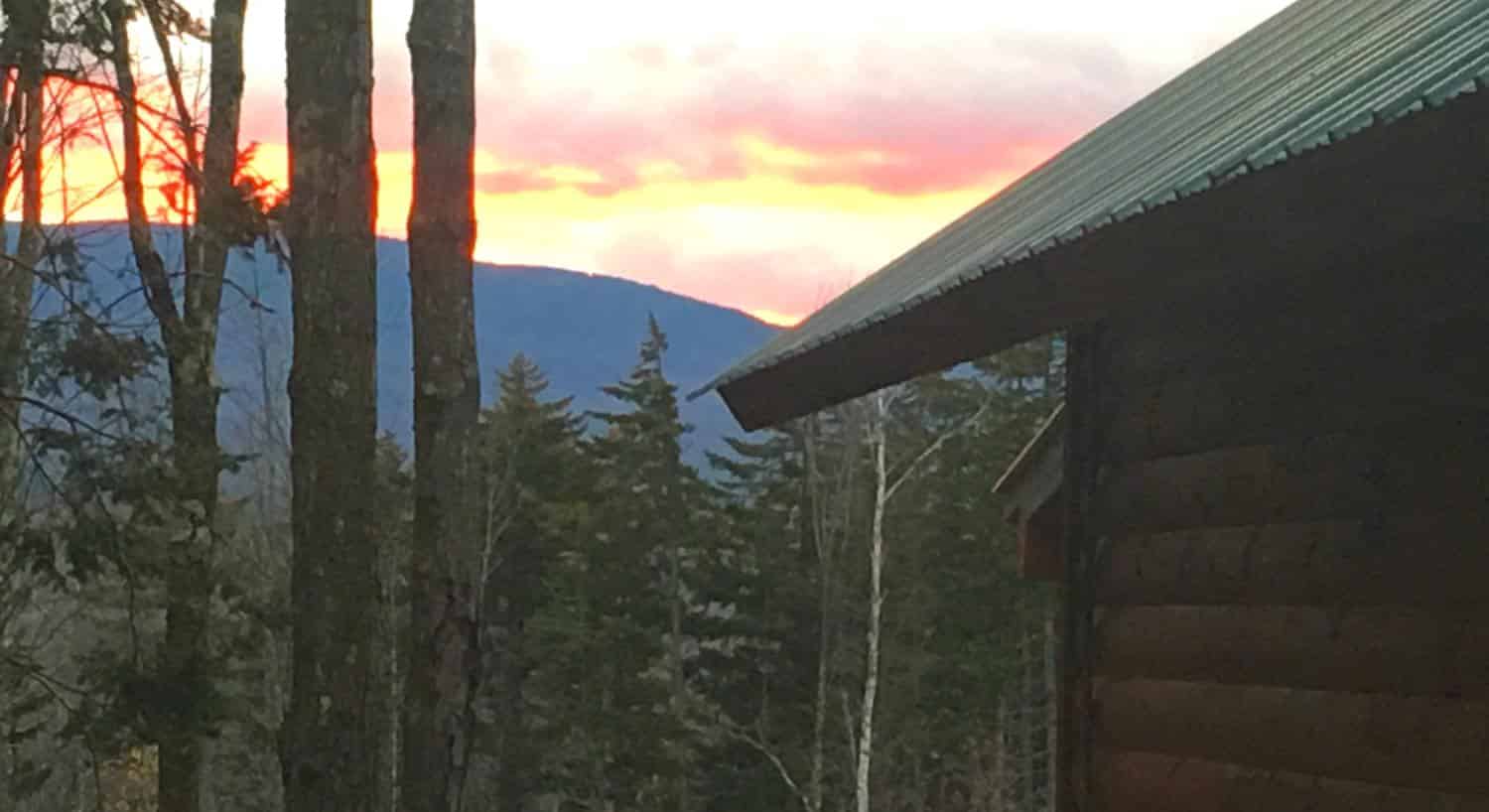 View from the side of a cabin of the sunset sky over distant hills and pine trees
