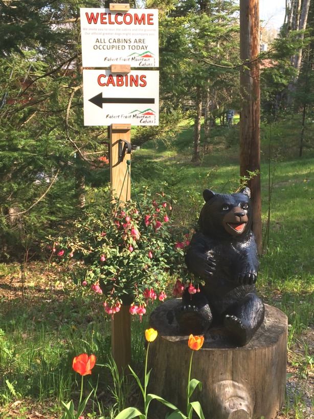 Painted carved bear on a tree stump surrounded by flowers and a directional sign to the cabins