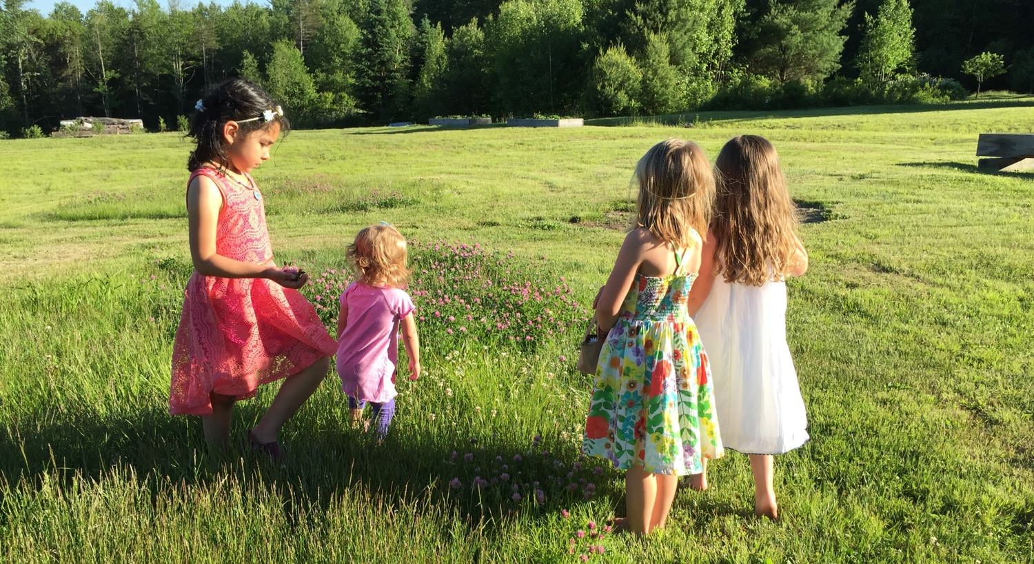 Four young girls wearing sundresses and playing in the grass 