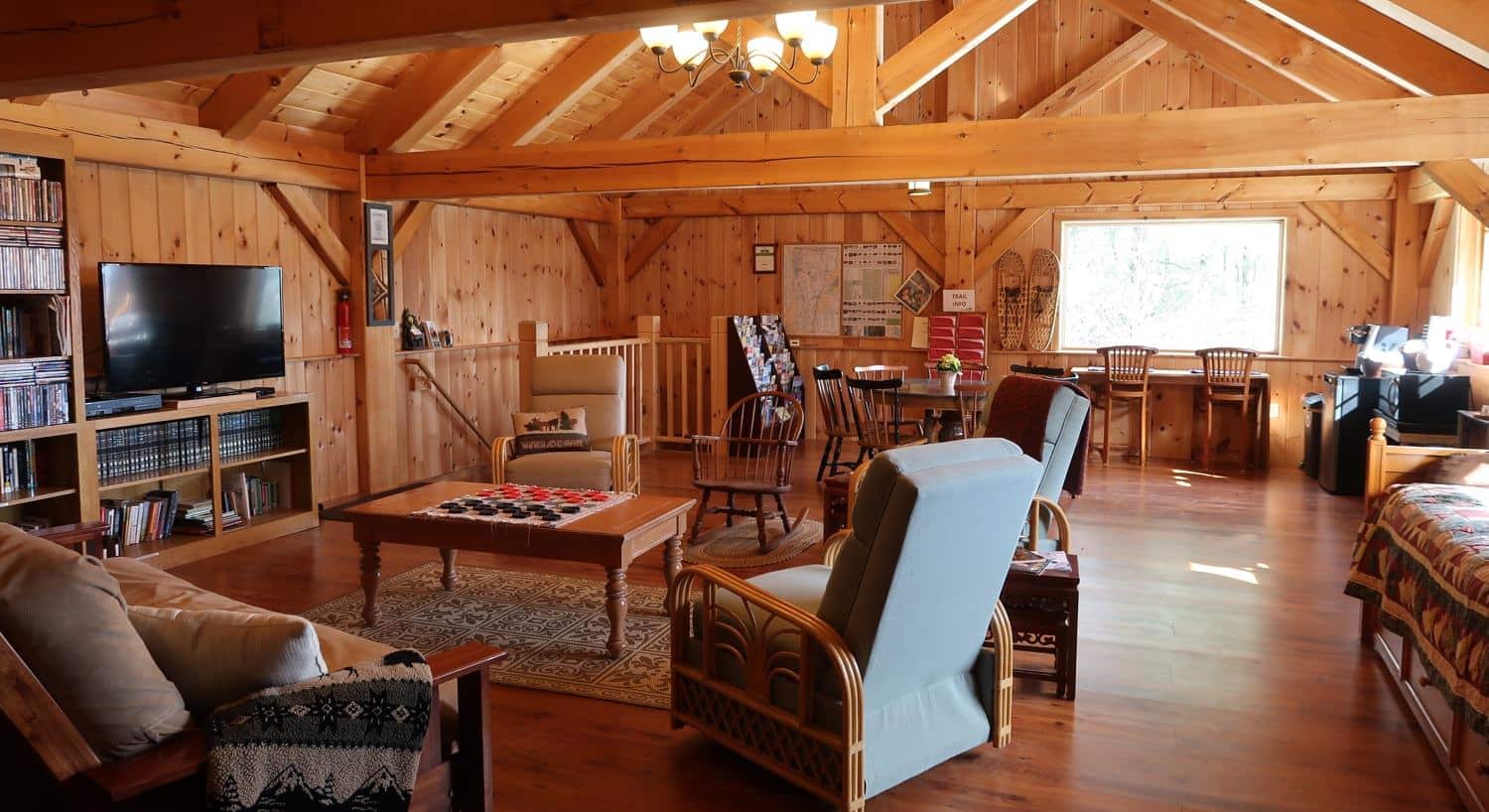 Inside the wooden community cabin with furniture, TV, books, games, dining tables and chairs and bar seating under the window