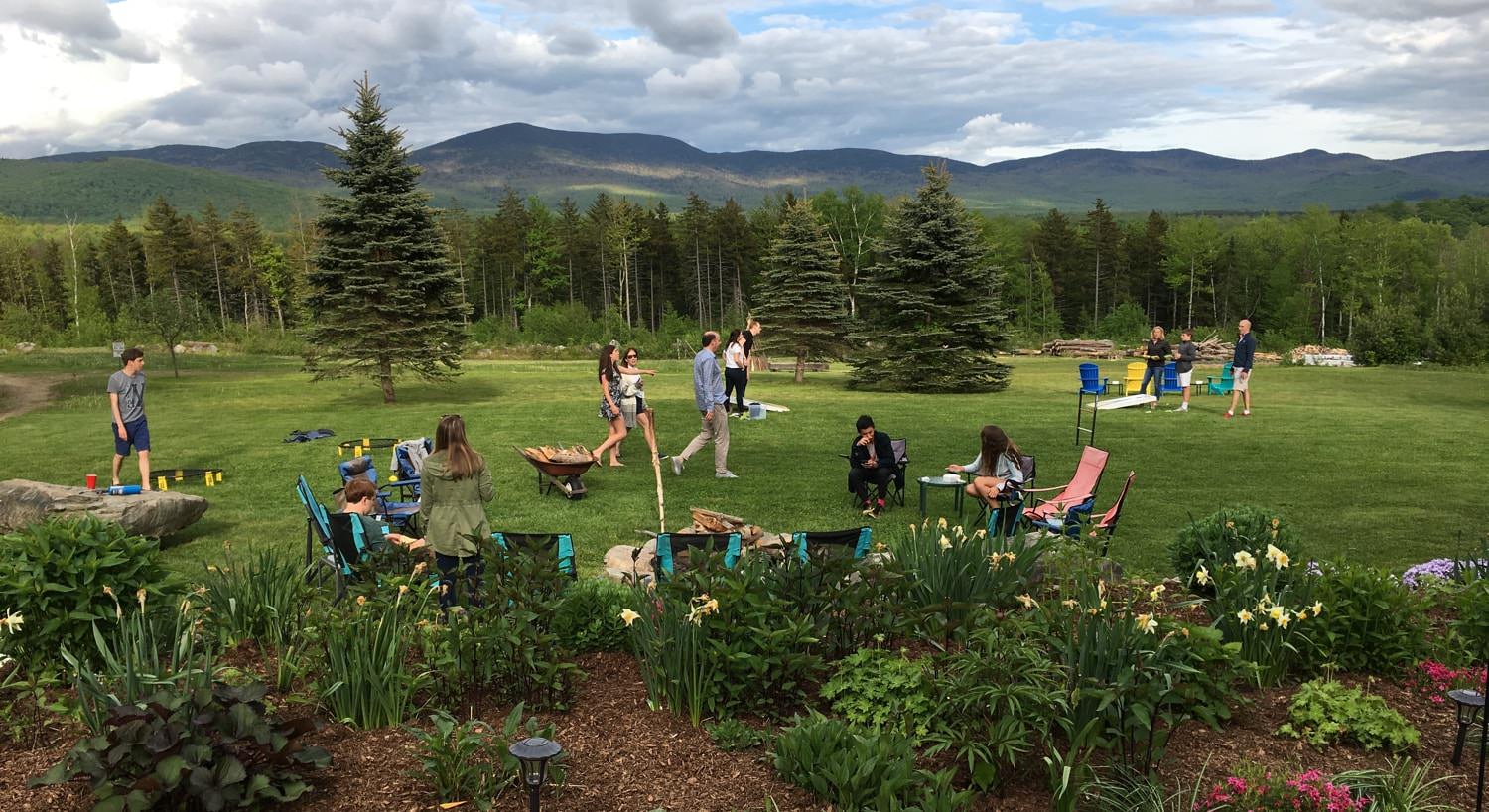 Several people in the common area enjoying yard games and the campfire surrounded by pine trees and distant hills