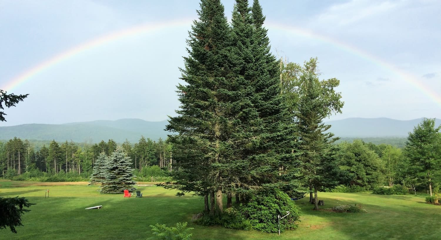 Gorgeous rainbow arced over the properties green grass, trees and distant hills