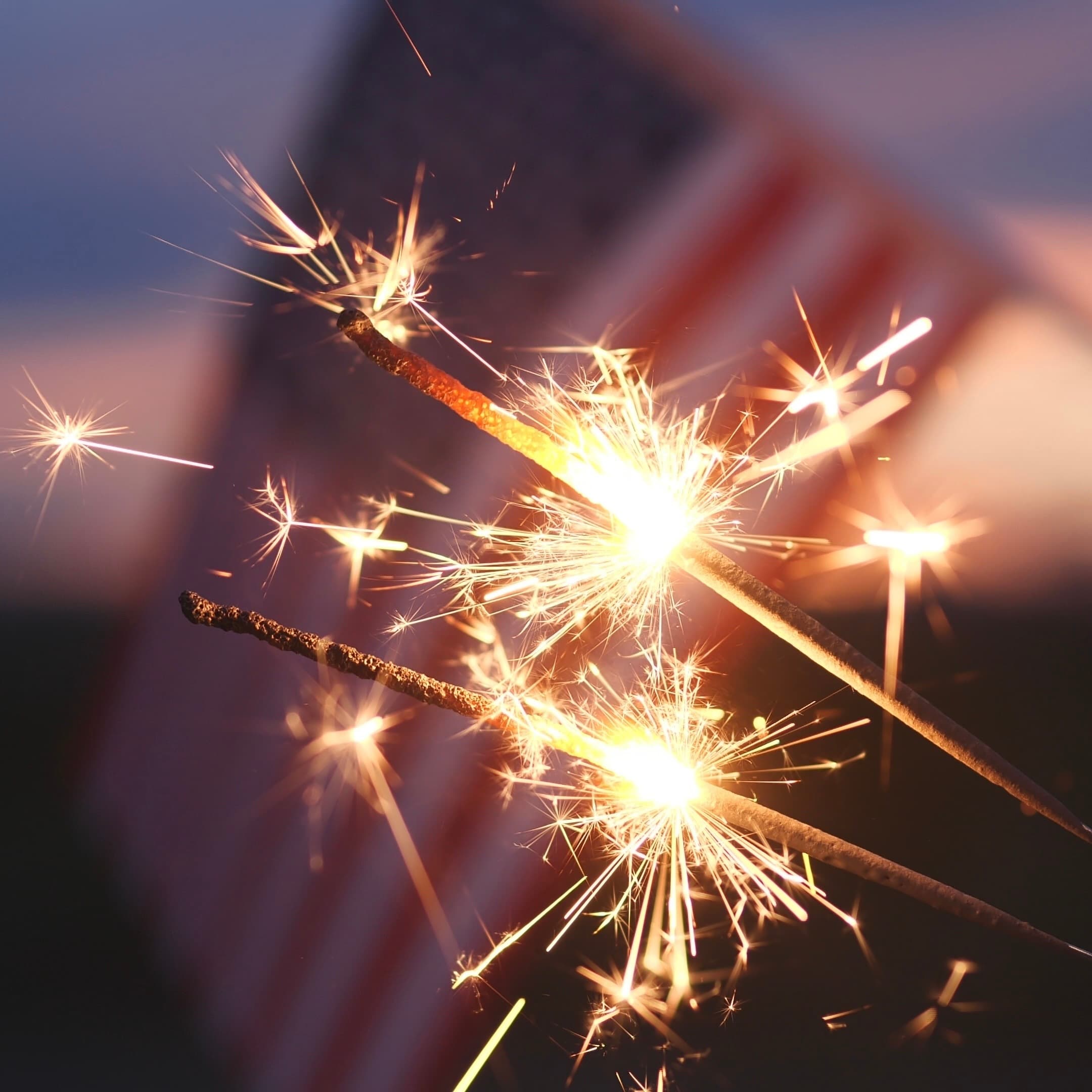 Sparklers ignite against a blurred backdrop of an American flag.