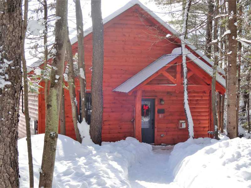A cozy timber-frame cabin with reddish-brown wood siding nestled in a serene, snow-covered forest during winter at Robert Frost Mountain Cabins in Ripton, Vermont.