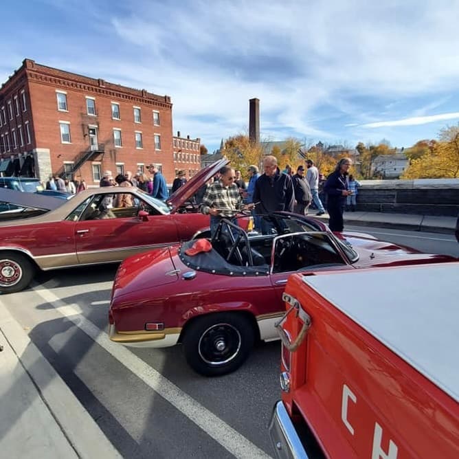 A crowd admires classic cars at a car show on a sunny day.