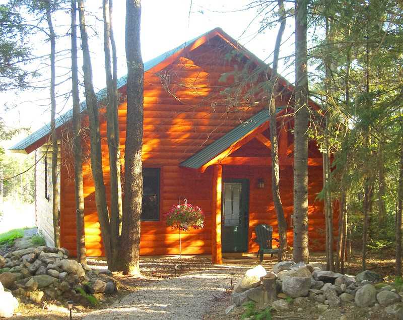 A cozy, artisan-crafted timber-frame cabin with warm wood siding tucked away in a sunny, wooded forest at Robert Frost Mountain Cabins in Vermont.
