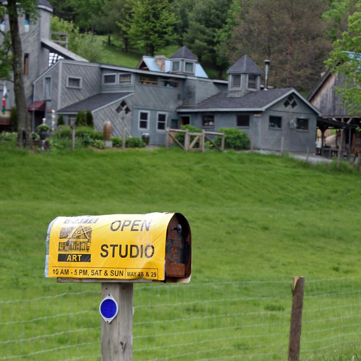A mailbox displaying an "Open Studio" sign stands in front of a unique, multi-level building surrounded by greenery.