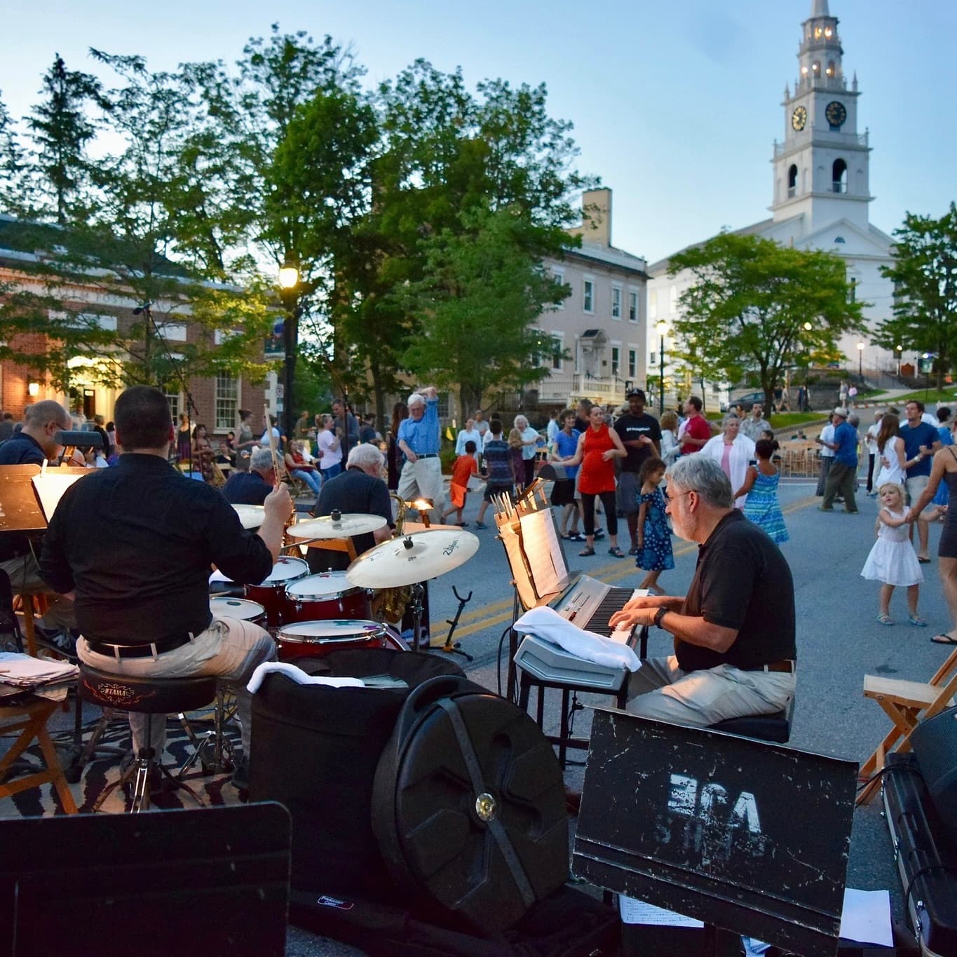 A live band plays music in a lively outdoor setting as people dance and enjoy the evening near a historic building.