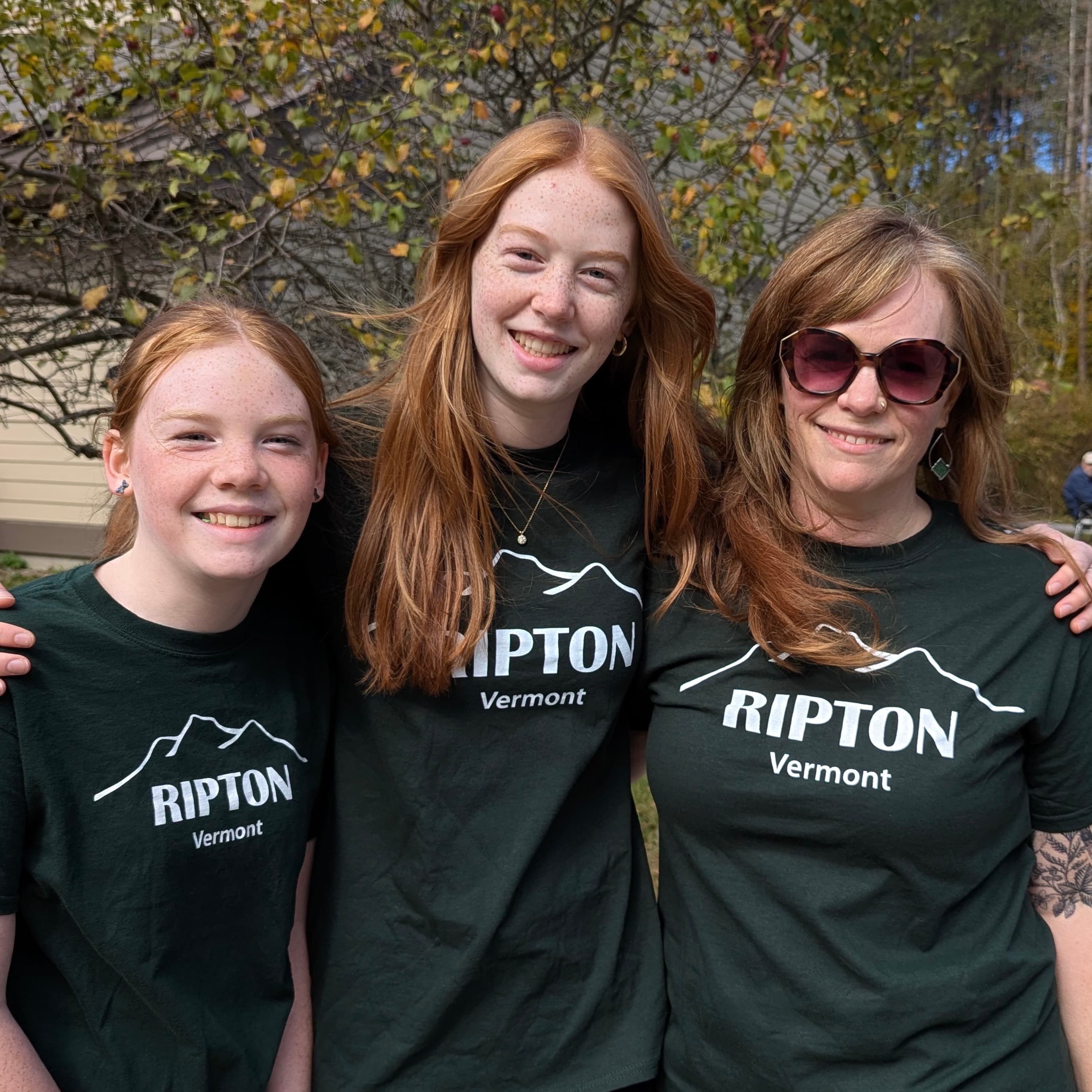 Three women wearing matching black t-shirts that say "RIPTON Vermont" pose together outdoors.