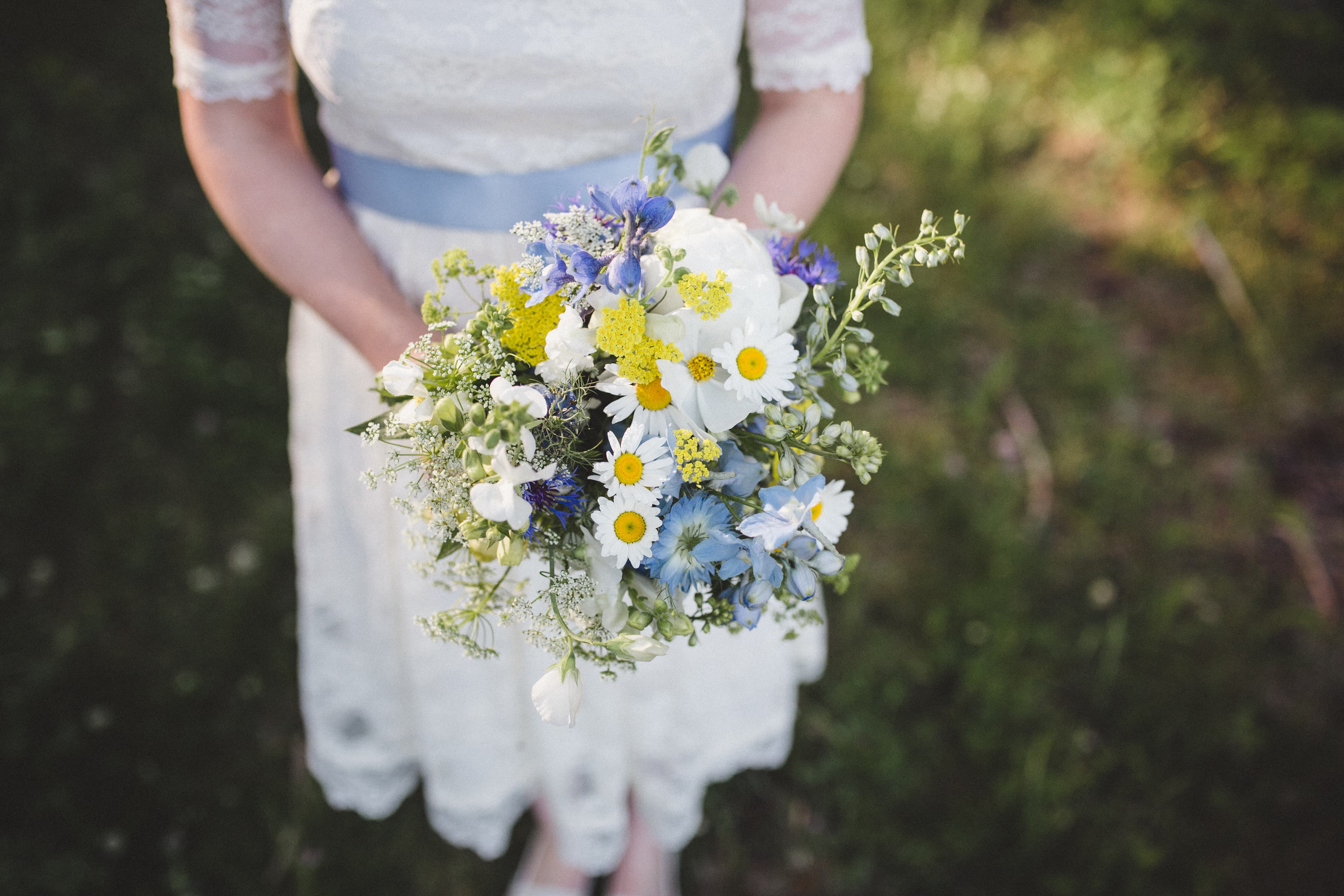 A person in a white lace dress holds a colorful bouquet of flowers.