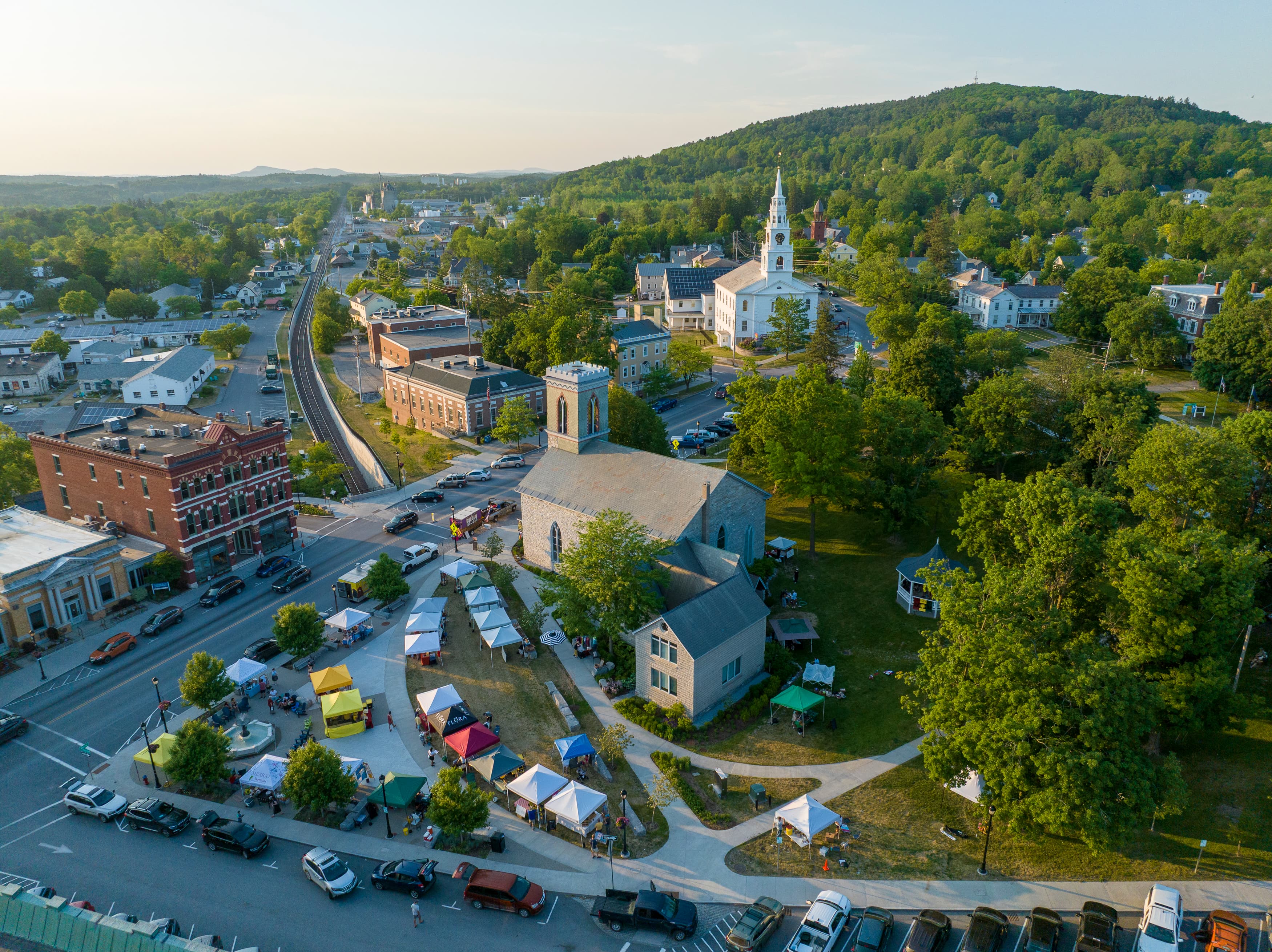 Aerial view of a small town with a church, green spaces, and a market area surrounded by hills.