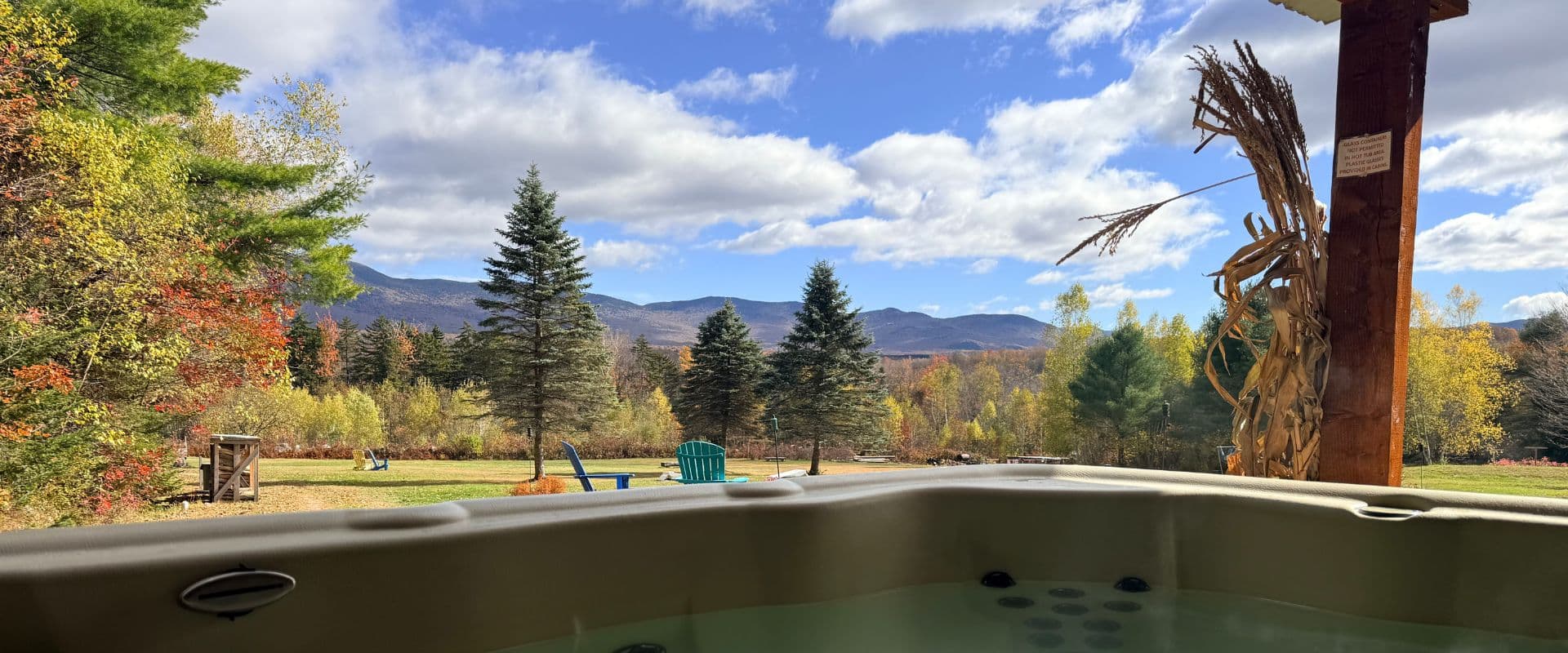 View from a hot tub overlooking a colorful autumn landscape and distant mountains under a partly cloudy sky.