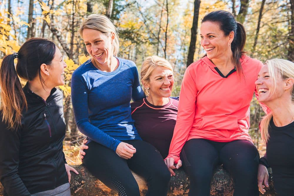 Five women laughing and enjoying each other's company outdoors in a forest setting during autumn.