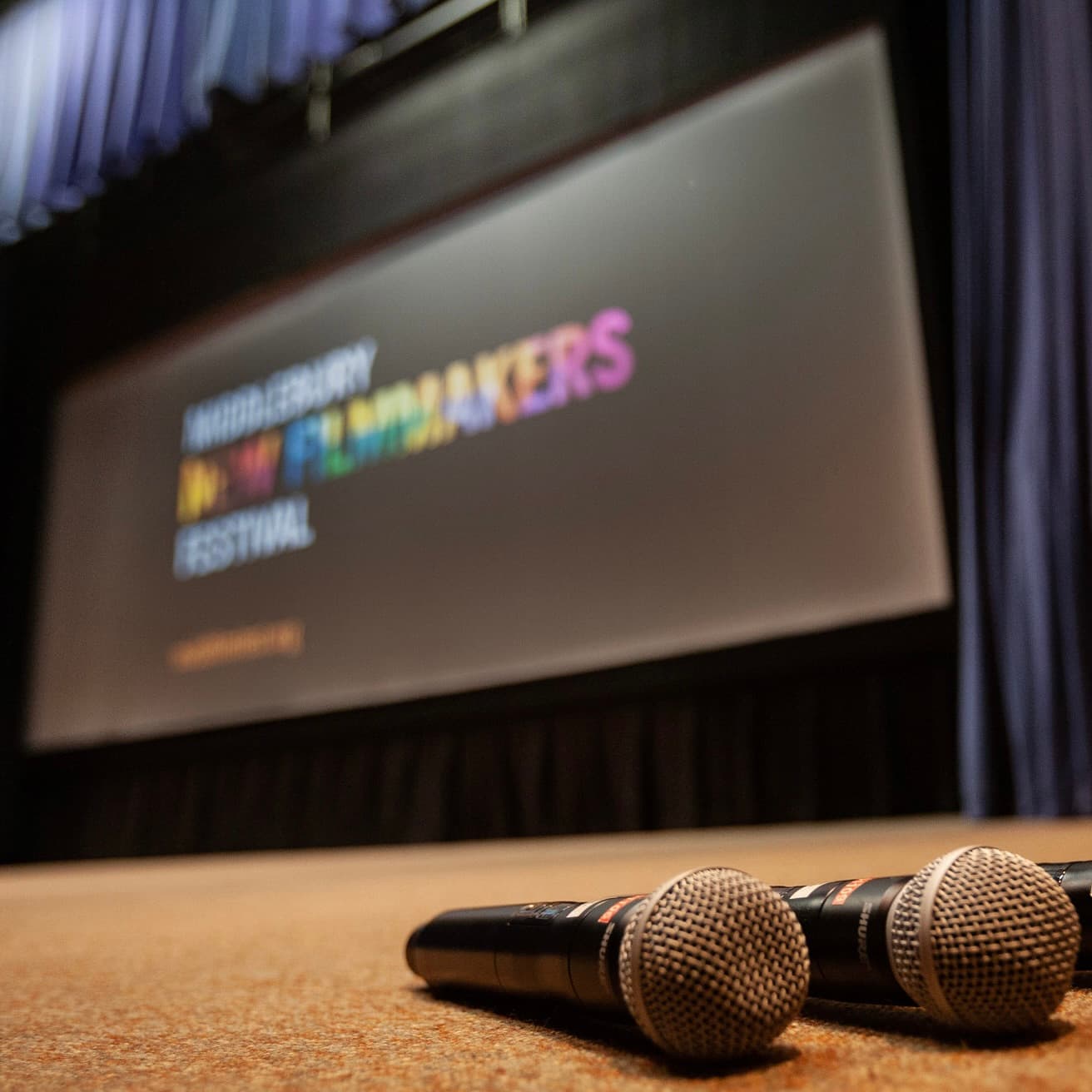 Two microphones are positioned on the stage in front of a backdrop featuring "Middlebury New Filmmakers Festival."