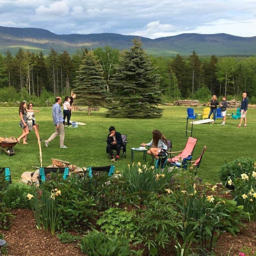 A group of people enjoys a gathering in a green field surrounded by trees and mountains.