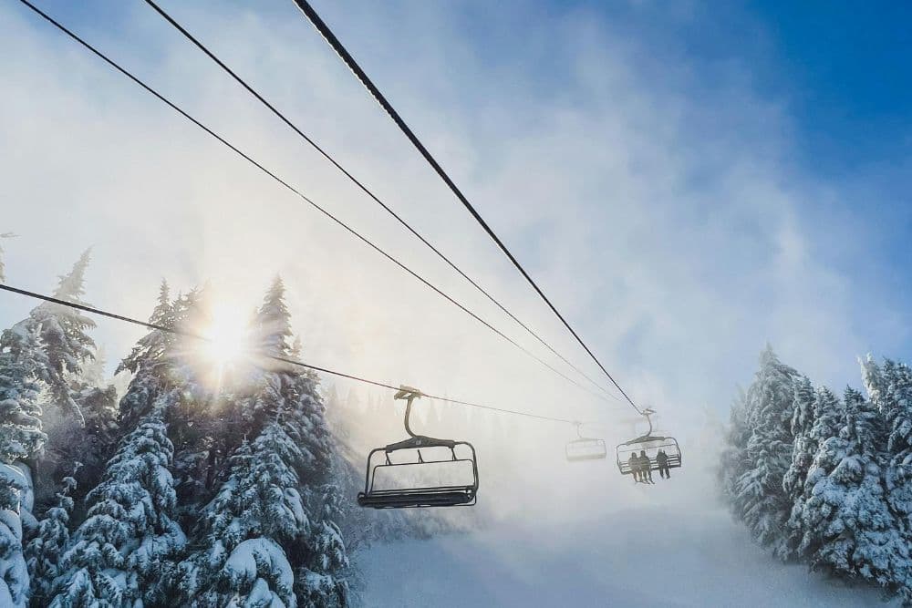 Ski lifts ascend through misty, snow-covered trees under a bright sky.