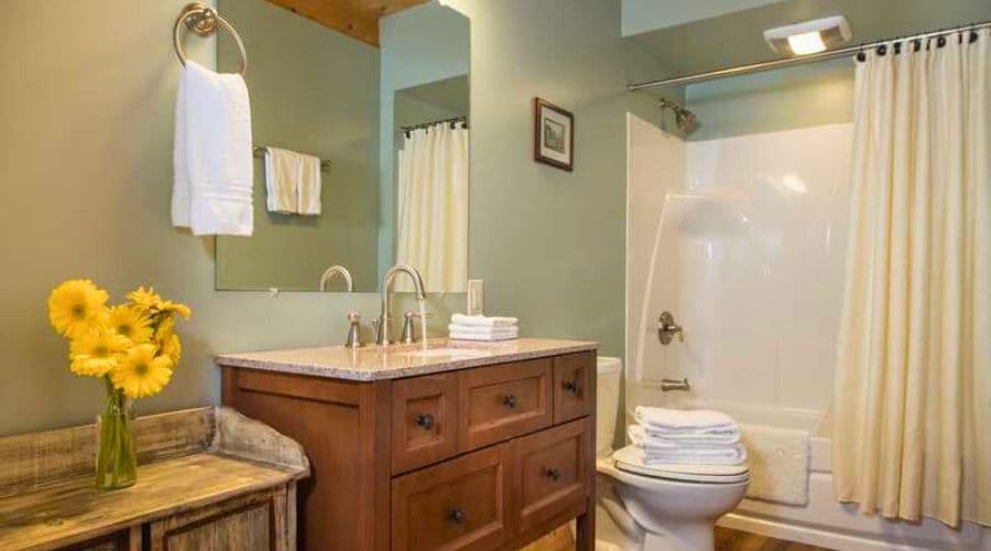 A neatly arranged bathroom featuring a wooden vanity, a shower/tub combo, and a vase of yellow flowers.