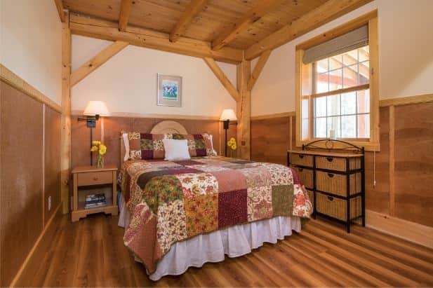 Blackberry Bend guest room, bed with colorful quilt, two nightstands with lamps, wicker chest of drawers and window