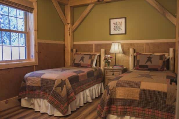 Evening Star guest room with wood floor and ceiling, center nightstand with lamp flanked by two beds with rustic quilt bedding