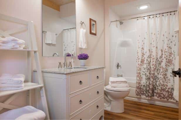 Hemlock Hideaway cabin's guest bath, wood floor, tub/shower, white vanity with mirror and ladder shelving with white towels