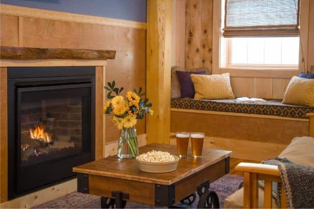 Hemlock Hideaway cabin's living area with fireplace, window and window seat, and coffee table topped with popcorn and beer