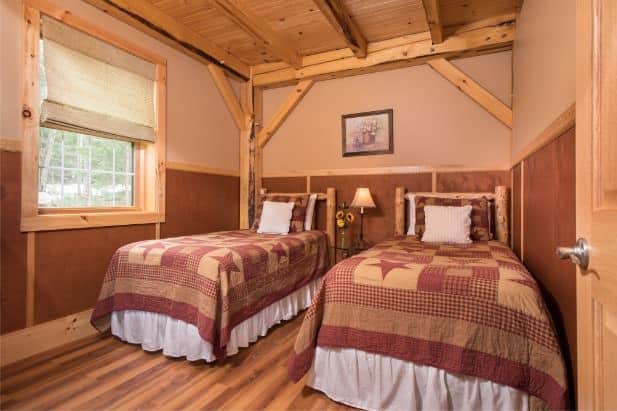 Owl's Branch guest room, two rustic beds flanking nightstand with lamp, wood floor and window