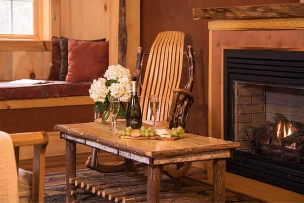 Owl's Branch living area, window with seat, fireplace, rocking chair, rustic coffee table topped with wine, grapes, crackers and cheese