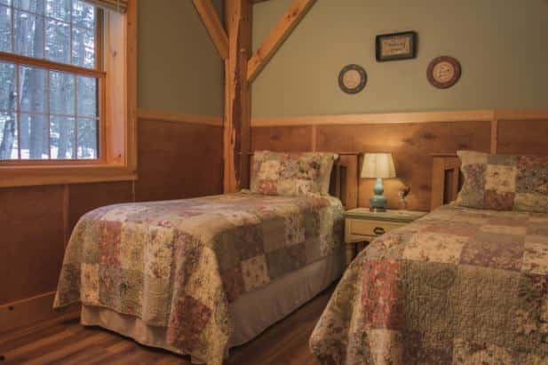 Peak Perspective guest room, two beds with pastel quilt flanking nightstand with lamp, light green walls, wood floor and window