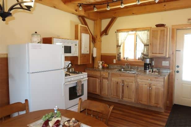 Sunrise Vista Cabin's kitchen with wood floor, ceiling and cabinets, warm beige walls, kitchen sink window and white appliances