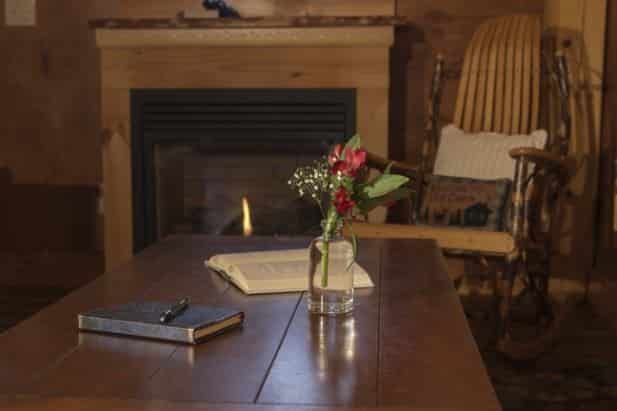 Sunrise Vista coffee table topped with guest book and flowers and a rustic rocking chair and fireplace in the background