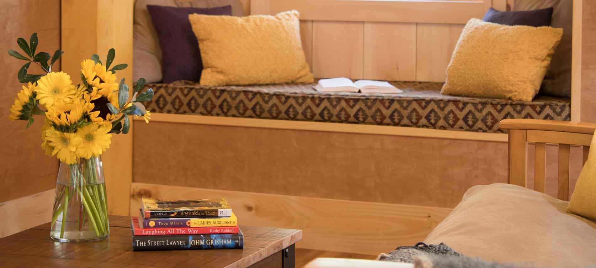 Close up view of built-in window seat and coffee table topped with fresh yellow flower and a stack of fictional books