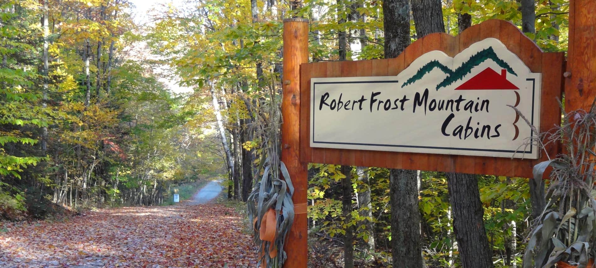 Wooded entrance sign that says, Robert Frost Mountain Cabins, and a road covered with fallen leaves and surrounded by trees