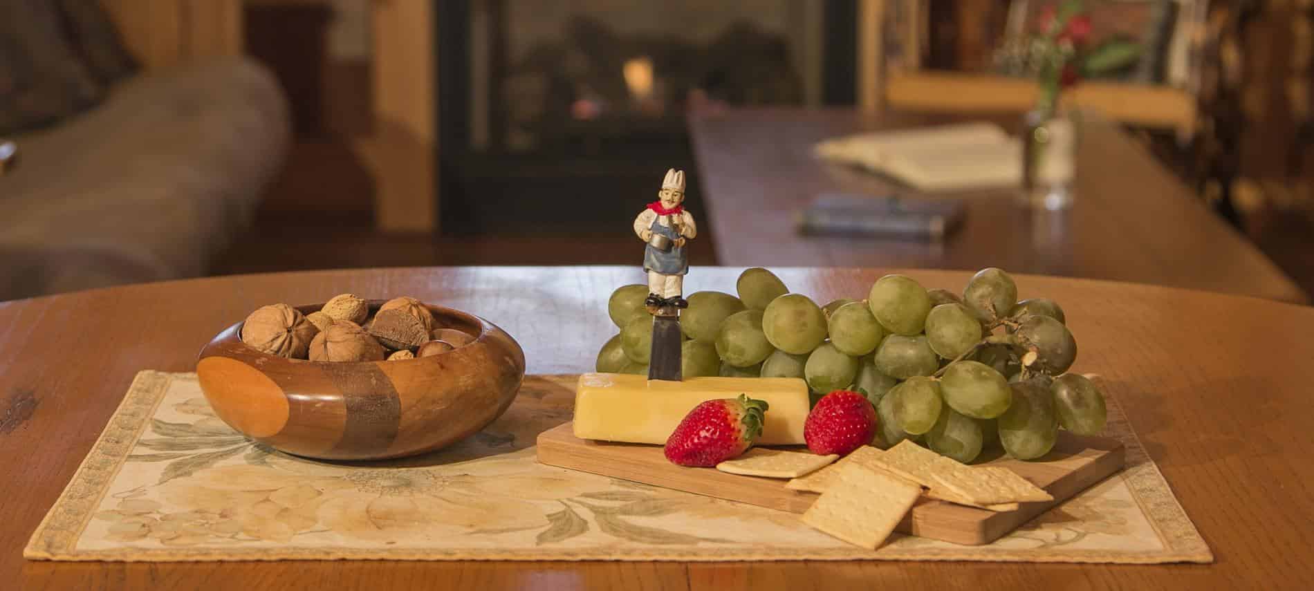 Dining table topped with bowl of nuts, green grapes, red strawberries, and cheese and crackers