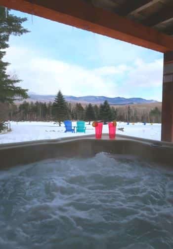 View from a bubbling hot tub of snow-covered ground, pine trees and distant hills