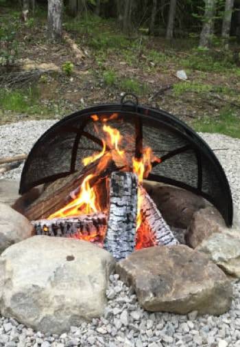 Campfire surrounded by large rocks and gravel with trees in the background