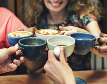 Women sitting a table clinking pottery cups filled with hot cocoa